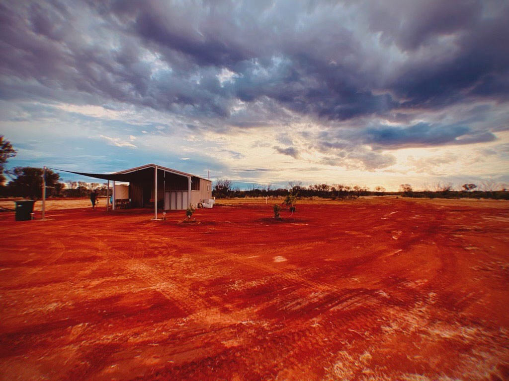 Small house with shadecloth verandah in a desert landscape with moody clouds above