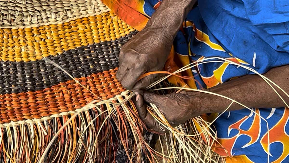 Aboriginal hands twisting pandanus into a yellow, orange, black radial mat